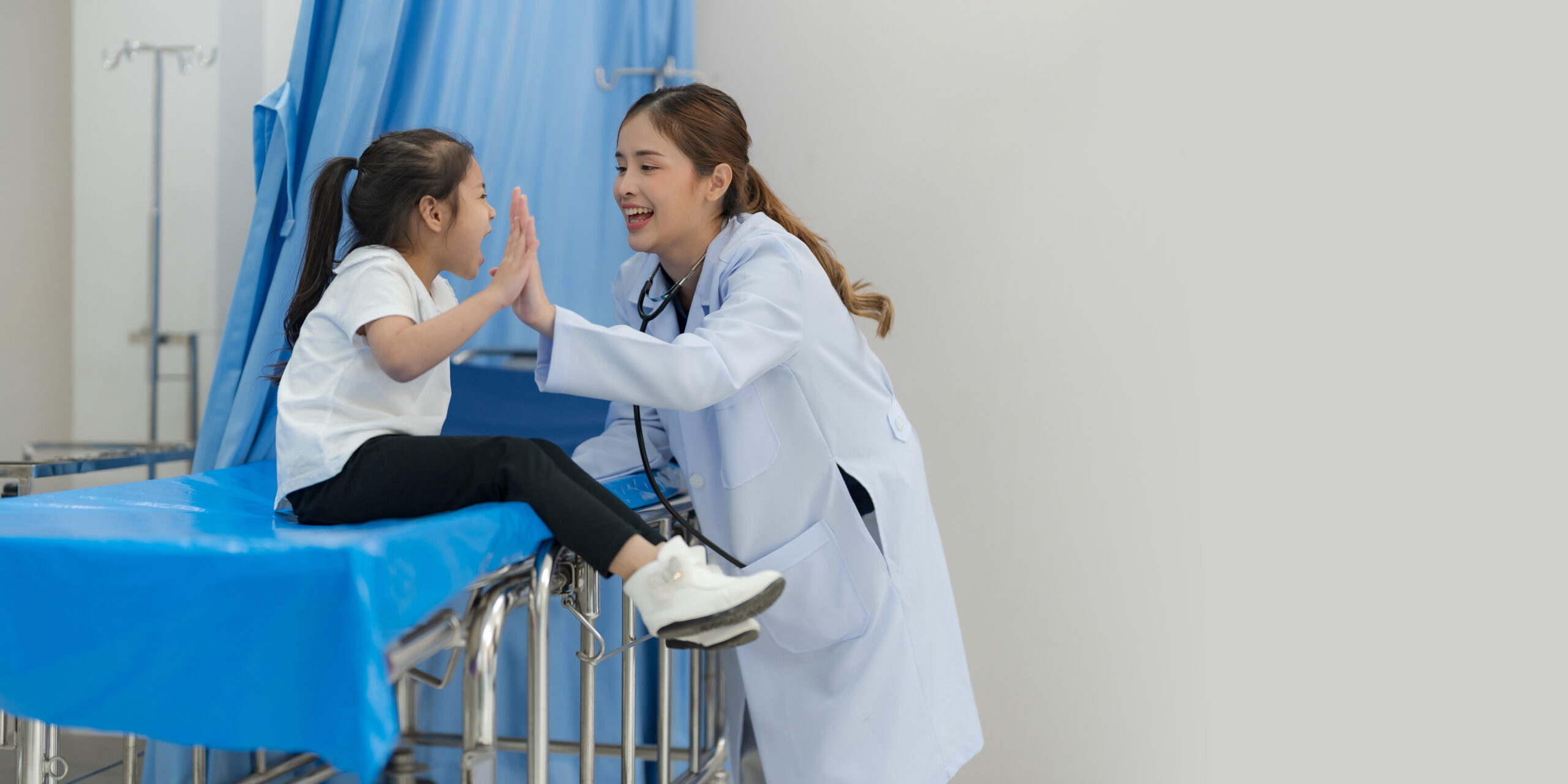The girl sits on the patient's bed for the doctor to examine the body.